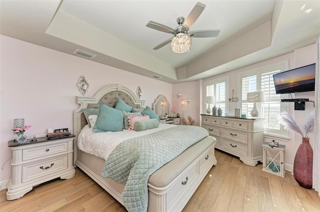 bedroom featuring ceiling fan, light hardwood / wood-style floors, and a tray ceiling