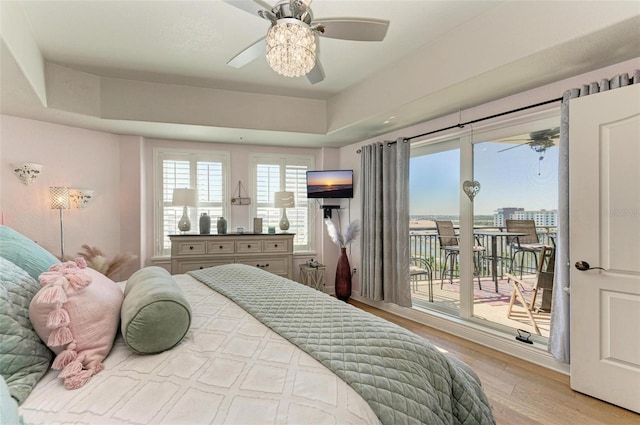 bedroom featuring a tray ceiling, access to exterior, ceiling fan, and light hardwood / wood-style floors