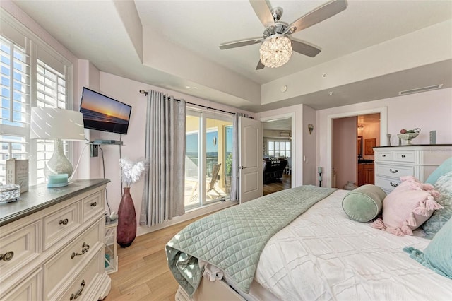 bedroom with ceiling fan, light wood-type flooring, a tray ceiling, and multiple windows