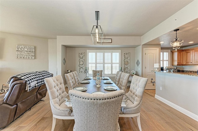 dining space featuring light wood-style flooring, a notable chandelier, and baseboards