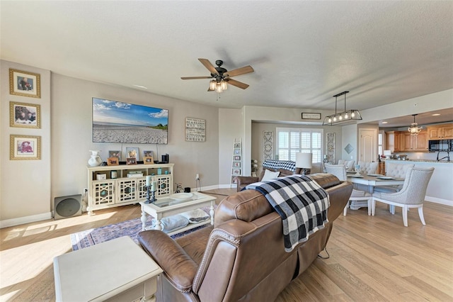 living area with light wood-style floors, baseboards, a ceiling fan, and a textured ceiling