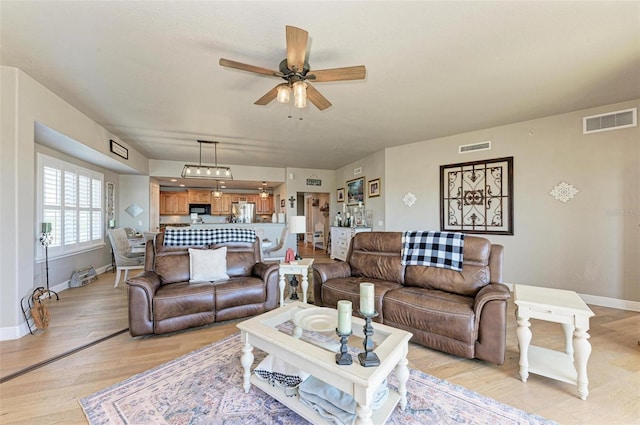living area featuring visible vents, baseboards, a ceiling fan, and light wood-style floors