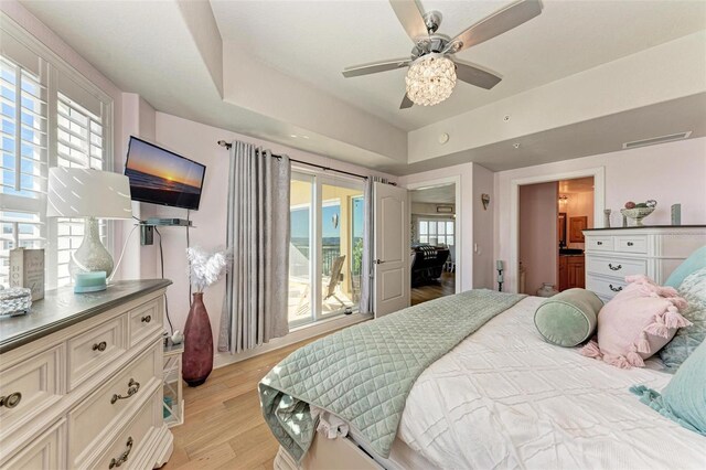 bedroom with light wood finished floors, visible vents, a tray ceiling, and ceiling fan