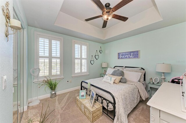 carpeted bedroom featuring a tray ceiling, baseboards, and ceiling fan