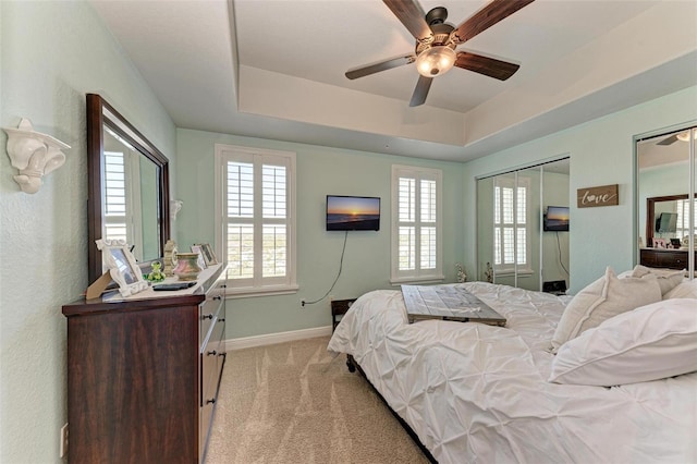 bedroom featuring baseboards, a raised ceiling, two closets, ceiling fan, and light colored carpet