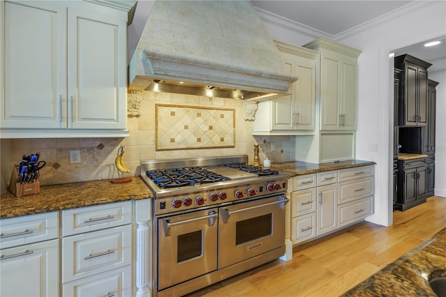 kitchen with premium range hood, crown molding, dark stone counters, range with two ovens, and decorative backsplash