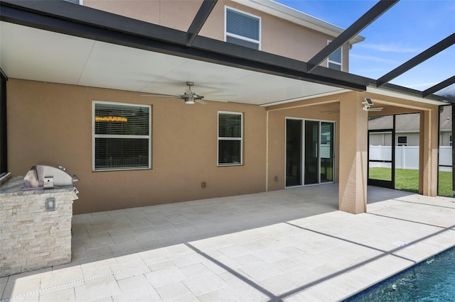 view of patio featuring an outdoor kitchen, glass enclosure, and ceiling fan