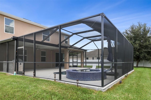 back of house featuring a lawn, glass enclosure, ceiling fan, a patio area, and an in ground hot tub