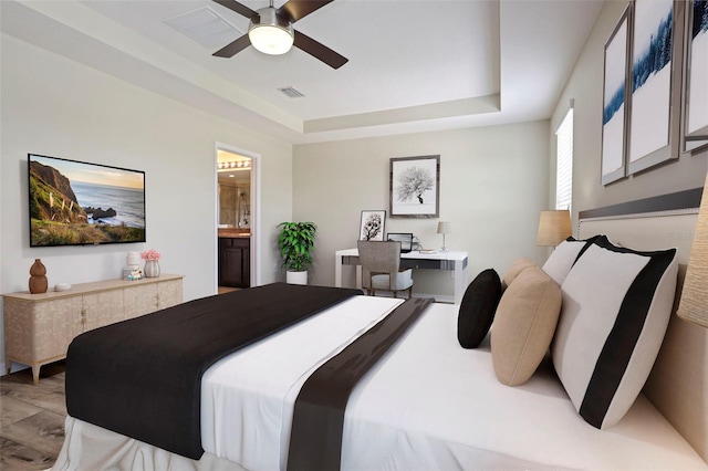 bedroom with a tray ceiling, ensuite bath, ceiling fan, and light hardwood / wood-style flooring