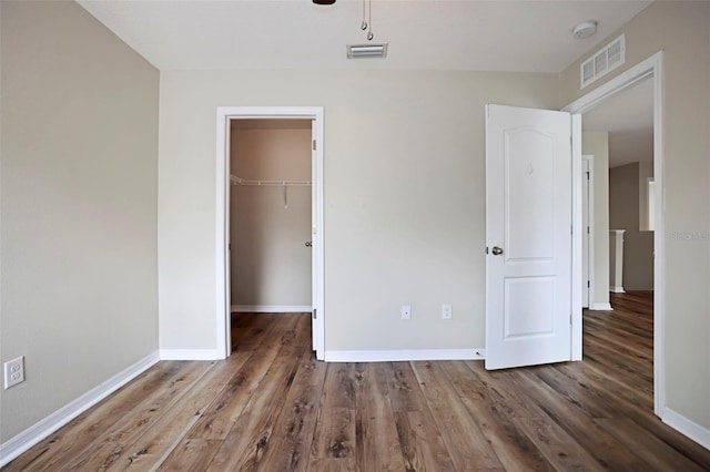 unfurnished bedroom featuring a walk in closet, a closet, and hardwood / wood-style flooring