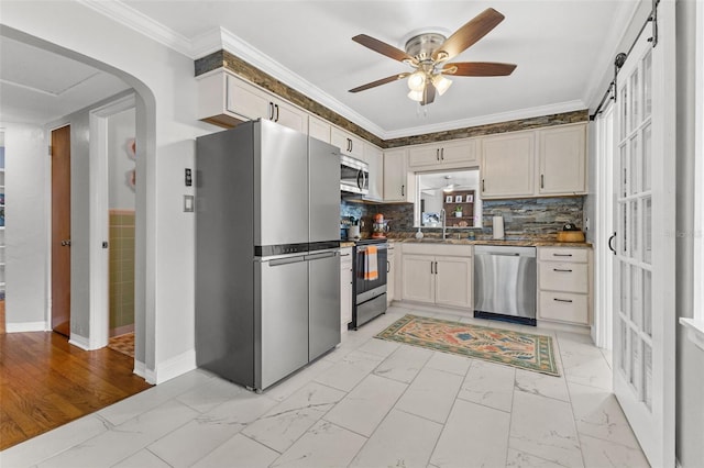 kitchen with appliances with stainless steel finishes, ceiling fan, crown molding, sink, and a barn door