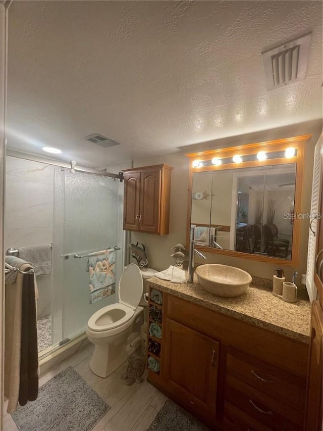 bathroom featuring a textured ceiling, vanity, hardwood / wood-style floors, toilet, and a shower with shower door