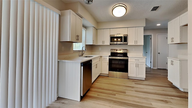 kitchen with white cabinets, sink, a textured ceiling, appliances with stainless steel finishes, and light hardwood / wood-style floors