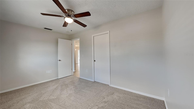 unfurnished bedroom with ceiling fan, a closet, light colored carpet, and a textured ceiling