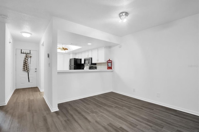 kitchen with white cabinets, black fridge, a textured ceiling, dark hardwood / wood-style flooring, and kitchen peninsula