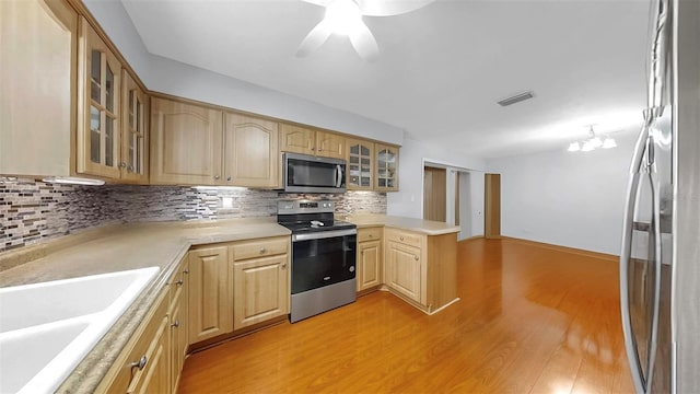 38919 3rd Ave, Zephyrhills, FL 33542 - kitchen featuring appliances with stainless steel finishes, a peninsula, light wood finished floors, decorative backsplash, and light countertops