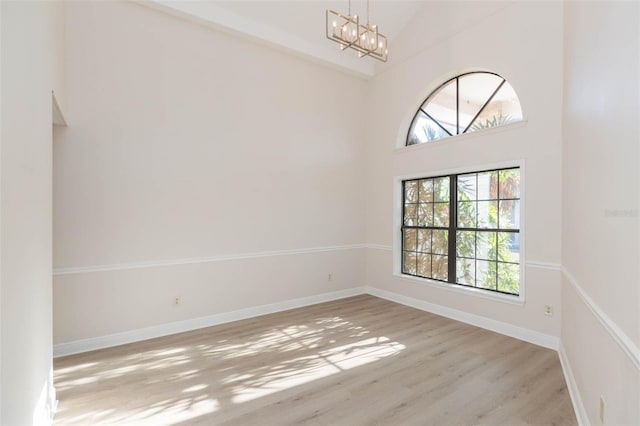 empty room featuring high vaulted ceiling, light hardwood / wood-style floors, and a notable chandelier