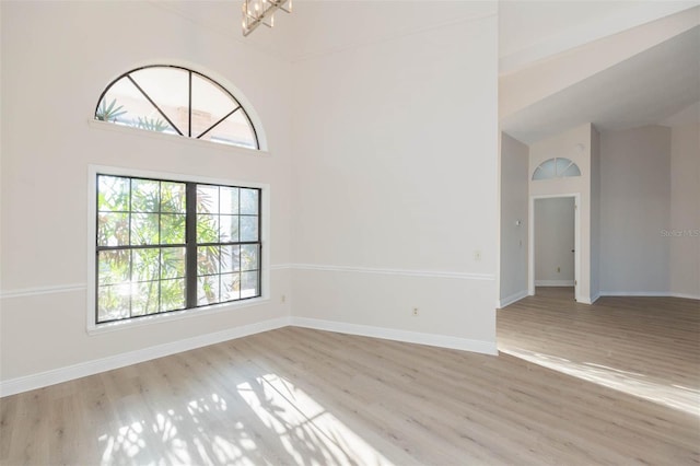 unfurnished room featuring a chandelier, light hardwood / wood-style floors, and high vaulted ceiling