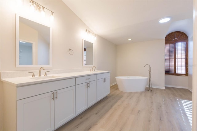 bathroom with a bathing tub, hardwood / wood-style floors, vanity, and vaulted ceiling