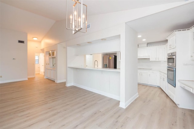 kitchen with white cabinets, vaulted ceiling, light wood-type flooring, appliances with stainless steel finishes, and a chandelier