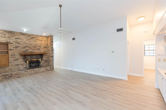 unfurnished living room featuring ceiling fan, light hardwood / wood-style floors, a towering ceiling, and a fireplace