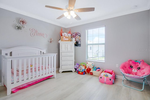 bedroom featuring ceiling fan, crown molding, a crib, and hardwood / wood-style flooring