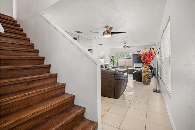 stairs with ceiling fan, tile patterned floors, and a textured ceiling