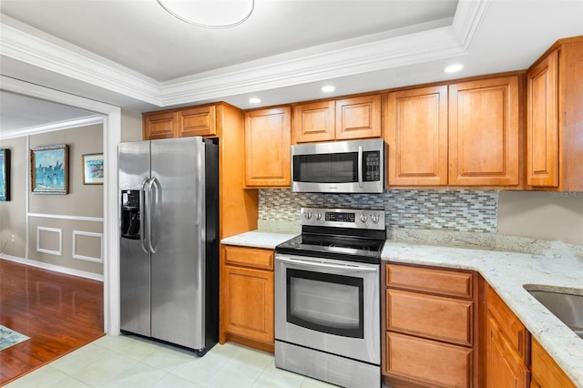 kitchen featuring stainless steel appliances, a raised ceiling, light stone counters, light hardwood / wood-style floors, and ornamental molding