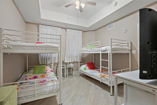 bedroom with ceiling fan, a raised ceiling, and light wood-type flooring