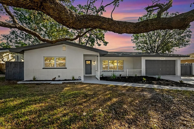 view of front facade with stucco siding, a garage, covered porch, and fence