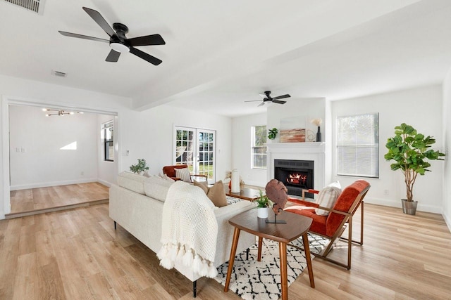 living area with light wood-type flooring, beamed ceiling, visible vents, a warm lit fireplace, and baseboards