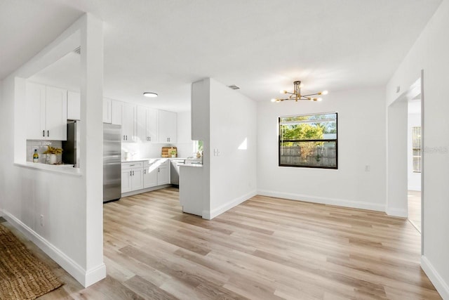 kitchen with an inviting chandelier, stainless steel built in refrigerator, light hardwood / wood-style floors, white cabinets, and decorative backsplash