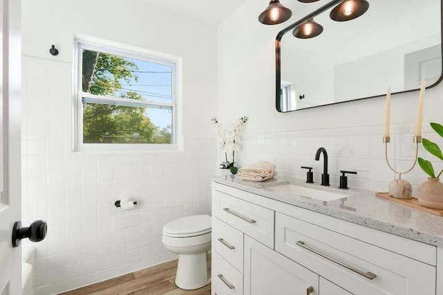 bathroom with tile walls, hardwood / wood-style floors, vanity, and toilet