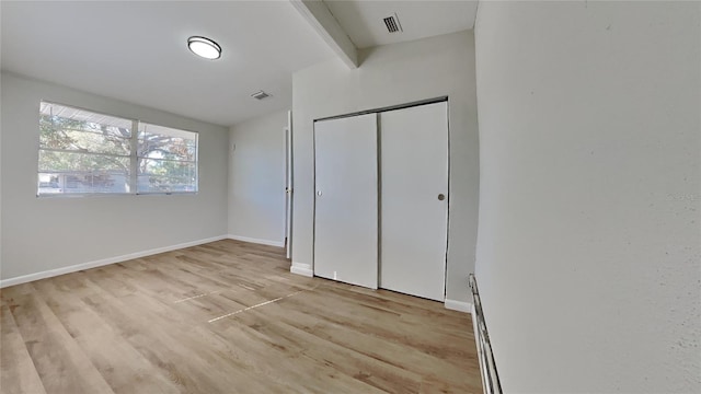 unfurnished bedroom featuring a closet, beamed ceiling, and light hardwood / wood-style floors