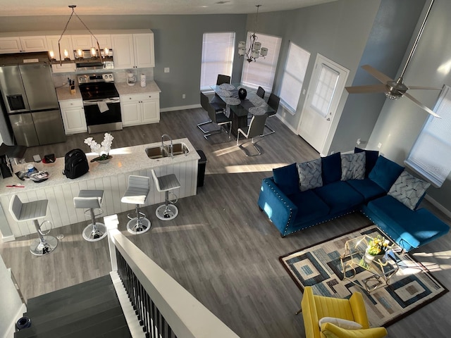 living room with a high ceiling, ceiling fan with notable chandelier, dark wood-type flooring, and sink