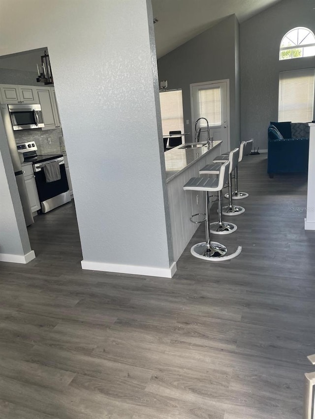 kitchen featuring dark wood-type flooring, stainless steel appliances, vaulted ceiling, a breakfast bar, and white cabinets