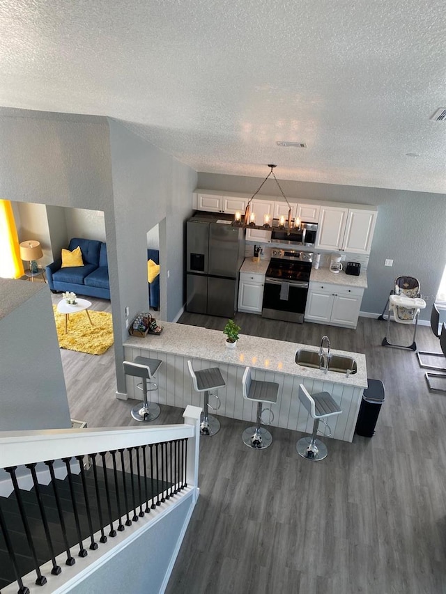 kitchen with white cabinetry, dark hardwood / wood-style floors, pendant lighting, a kitchen bar, and appliances with stainless steel finishes