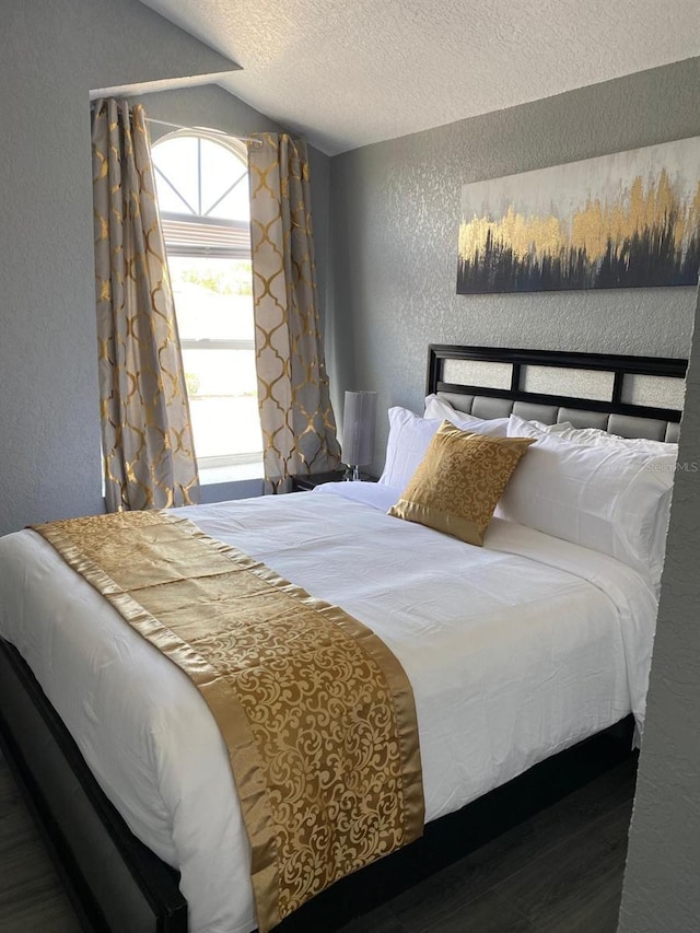 bedroom with a textured ceiling, hardwood / wood-style flooring, and lofted ceiling