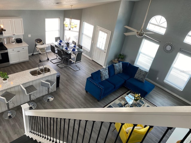 living room featuring dark hardwood / wood-style flooring, ceiling fan with notable chandelier, a textured ceiling, sink, and high vaulted ceiling