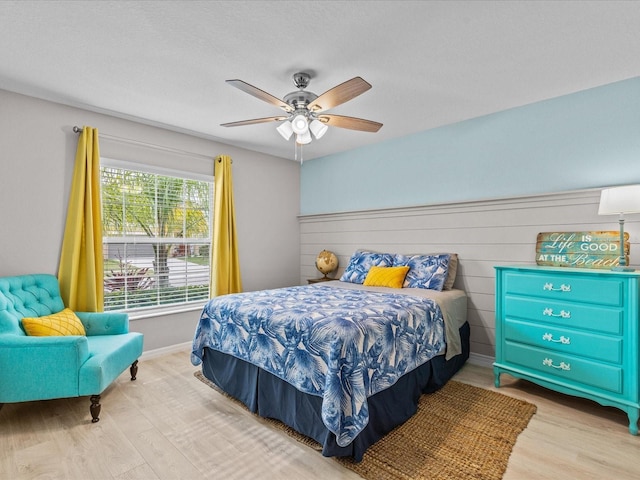 bedroom with ceiling fan, wooden walls, and light hardwood / wood-style floors