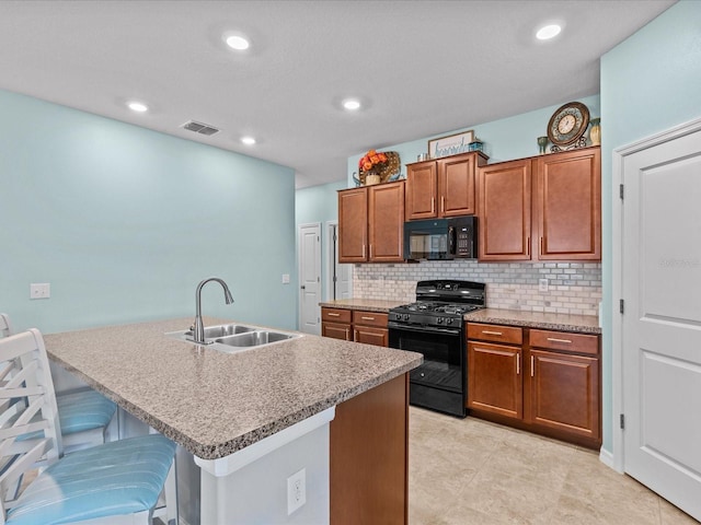 kitchen featuring backsplash, a kitchen island with sink, sink, black appliances, and a breakfast bar area