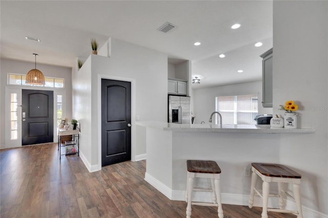 kitchen with a kitchen breakfast bar, dark hardwood / wood-style flooring, kitchen peninsula, stainless steel fridge, and gray cabinets