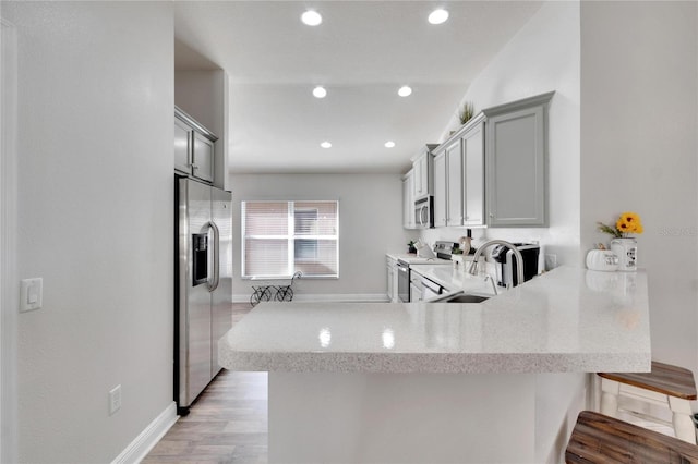 kitchen with sink, stainless steel appliances, light hardwood / wood-style flooring, kitchen peninsula, and a breakfast bar