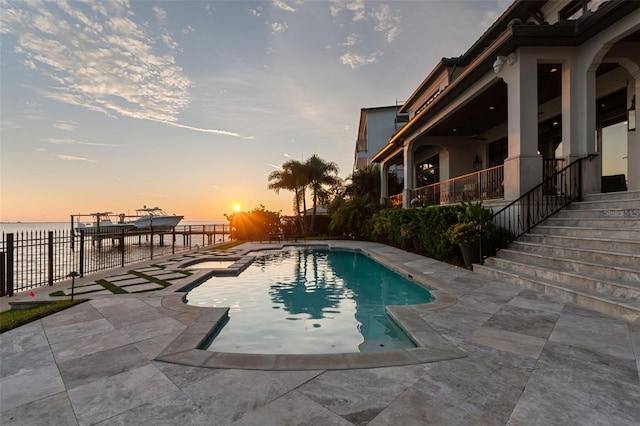 pool at dusk with a patio area and a water view