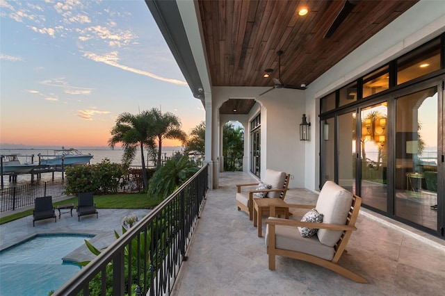 balcony at dusk with a water view and ceiling fan