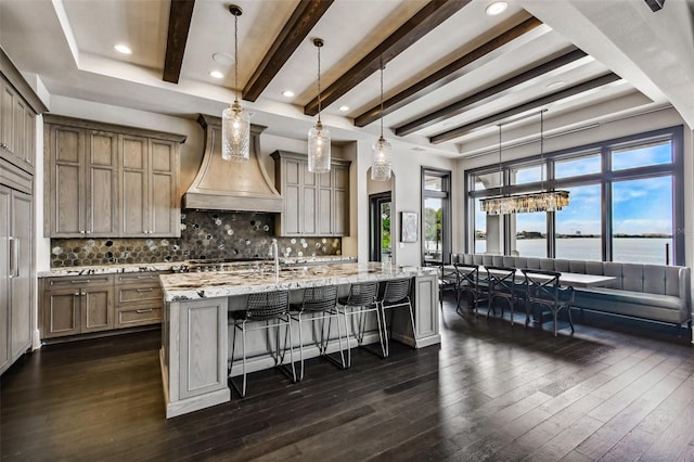 kitchen with light stone countertops, backsplash, custom range hood, pendant lighting, and a water view