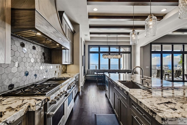 kitchen with dark wood-type flooring, range with two ovens, sink, hanging light fixtures, and decorative backsplash