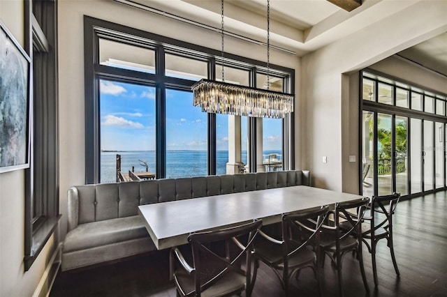 dining area with a healthy amount of sunlight, a water view, dark wood-type flooring, and an inviting chandelier