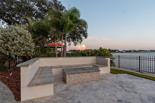 patio terrace at dusk featuring a water view and area for grilling