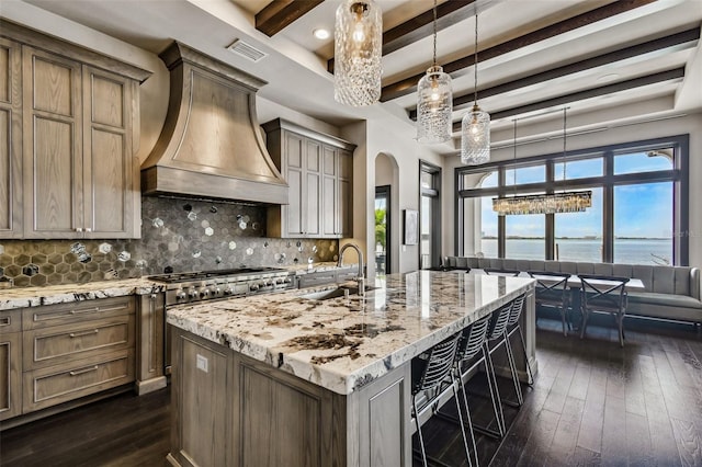 kitchen featuring tasteful backsplash, beamed ceiling, a kitchen island with sink, a water view, and custom exhaust hood